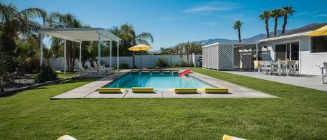 Un jardin avec une piscine, des chaises longues et un espace patio couvert.