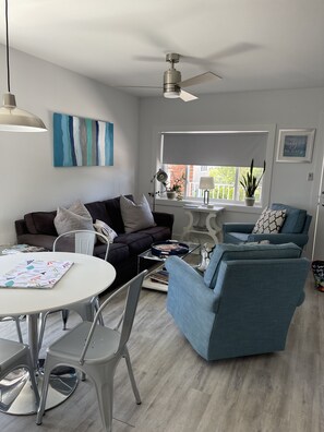 En moderne stue med en loftsvifte, to sofaer, et spisebord med stole og et vindue med udsigt over grønne områder.