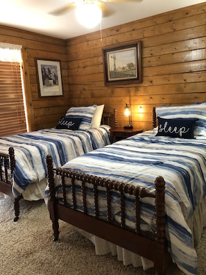 A bedroom with two wooden beds, each with striped bedding and pillows with the word "sleep" on them. There is a framed picture on the wall and a small table with a lamp between the beds. - YOUR SUMMER DESTINATION:  HUNT, TX  where the Guadalupe River awaits you! (Hunt)