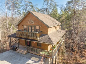 A two-story log cabin with a balcony and a deck, surrounded by trees.