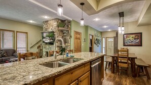 A kitchen with granite countertops, a stone backsplash, wooden cabinets, a built-in dishwasher, and pendant lighting. - Outdoor pool access, Private putt putt-Close to Pigeon Forge-outdoor kitchen-game room and  more.... (PIGEON)