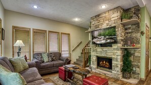 Una sala de estar acogedora con chimenea de piedra, un sofá confortable y un televisor montado encima.
