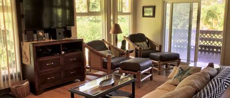 A spacious living room with a large sofa, two armchairs, a coffee table, and a TV on a wooden cabinet.