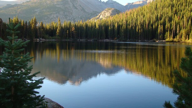 Un lac paisible, entouré d’une forêt dense et de montagnes.