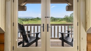 Een houten terras met twee zwarte Adirondack-stoelen en uitzicht op een meer en begroeiing.