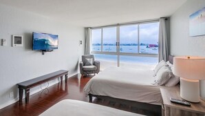 Ett hotellrum med ett stort fönster, en säng, en bänk, en stol, en tv och en lampa.