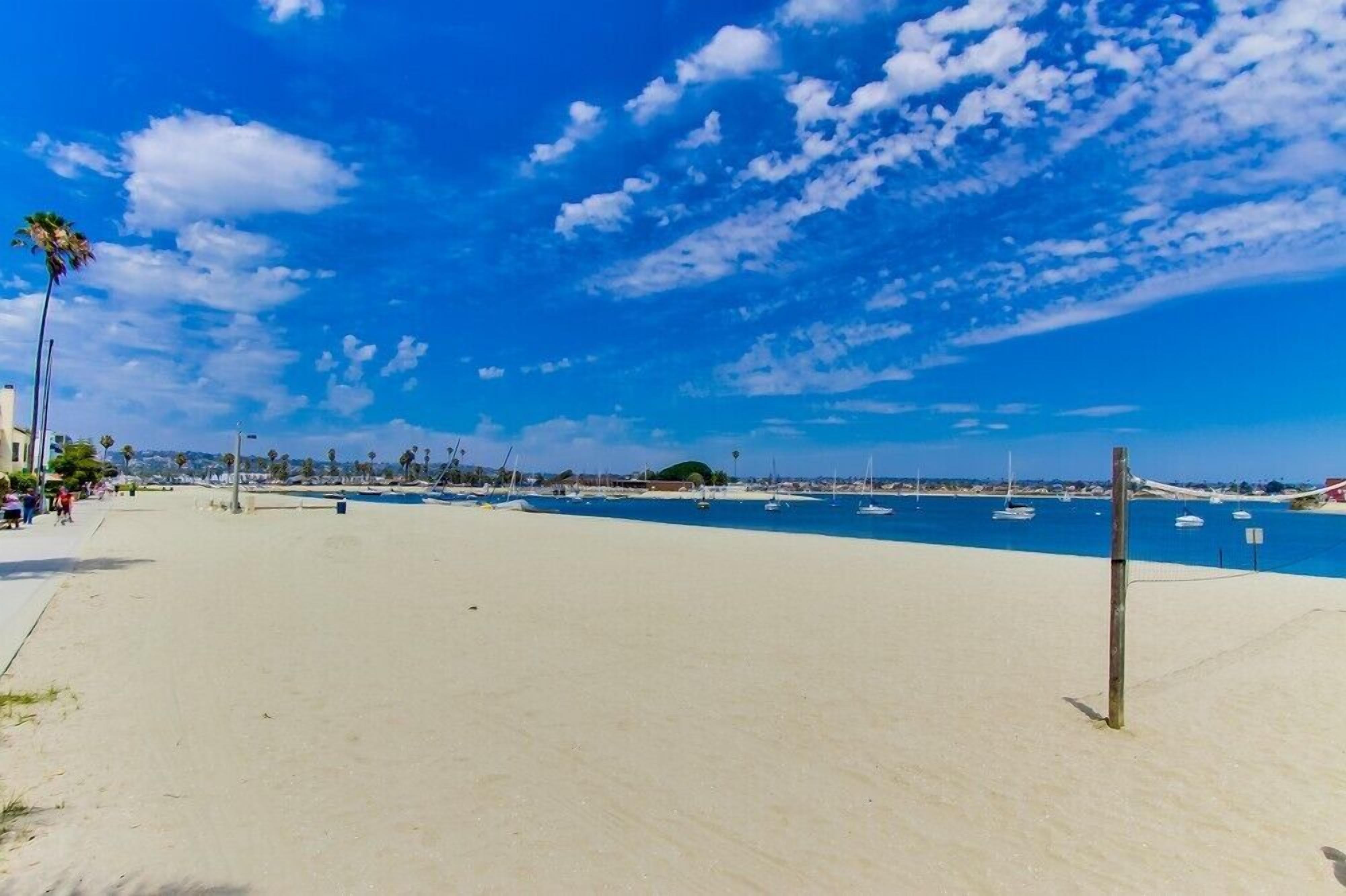 A beach with a clear sky, sandy shore, and boats in the water.
