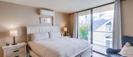 Un dormitorio con una cama grande, una mesita de noche con lámpara, una silla y vistas al exterior a través de un ventanal.