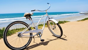 En vit cykel står parkerad på en sandstrand med havet i bakgrunden.