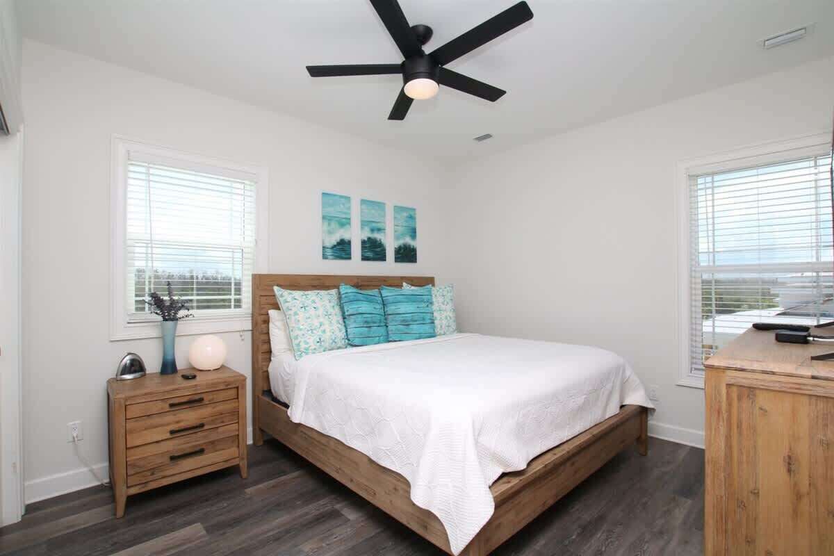 Une chambre à coucher avec un lit en bois, du linge de lit blanc, un ventilateur de plafond et une table de chevet avec une lampe.