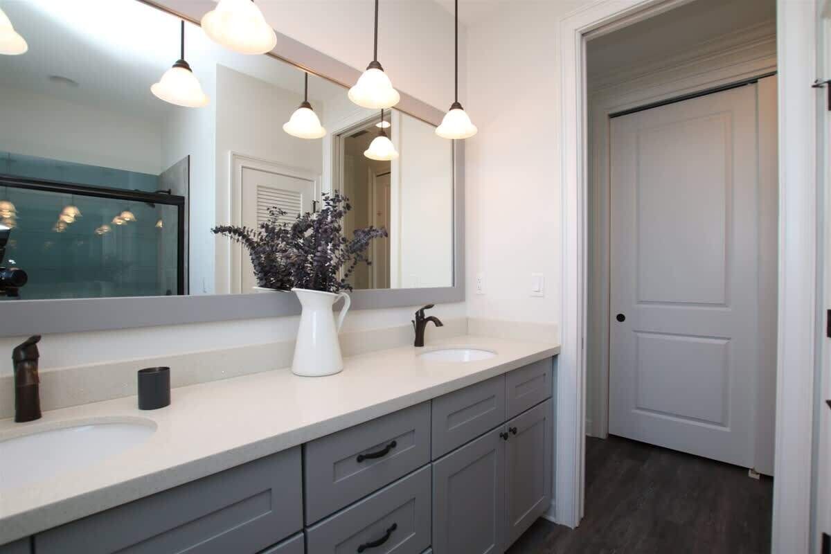A modern bathroom with a large mirror, pendant lights, a white sink, and grey cabinets.
