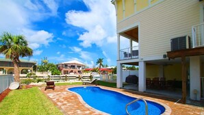 A swimming pool with a checkered pattern around it, a covered patio area, and a view of a building in the background. - Marathon 4BR | Pool, Dock & Near Sombrero Beach (Marathon)