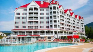A multi-story hotel with a red roof, balconies, and a swimming pool area with sun loungers. - River Walk Resort One bedroom Suite w/ balcony & mount view from 5th floor VIP. (Lincoln)