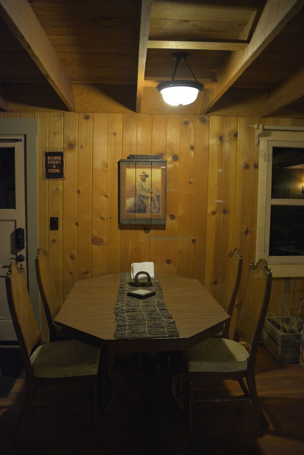 Habitación con paneles de madera, una mesa de comedor, sillas, un cuadro enmarcado y un letrero que indica la ocupación máxima.