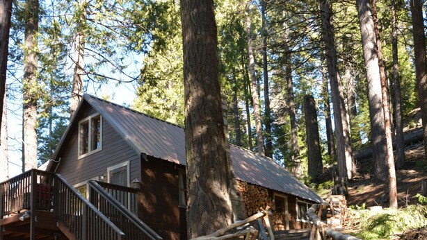 A cabin with a wooden deck, stone steps, and a metal railing.
