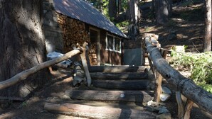 A rustic wooden staircase leading to a stone building with a metal roof, surrounded by trees.