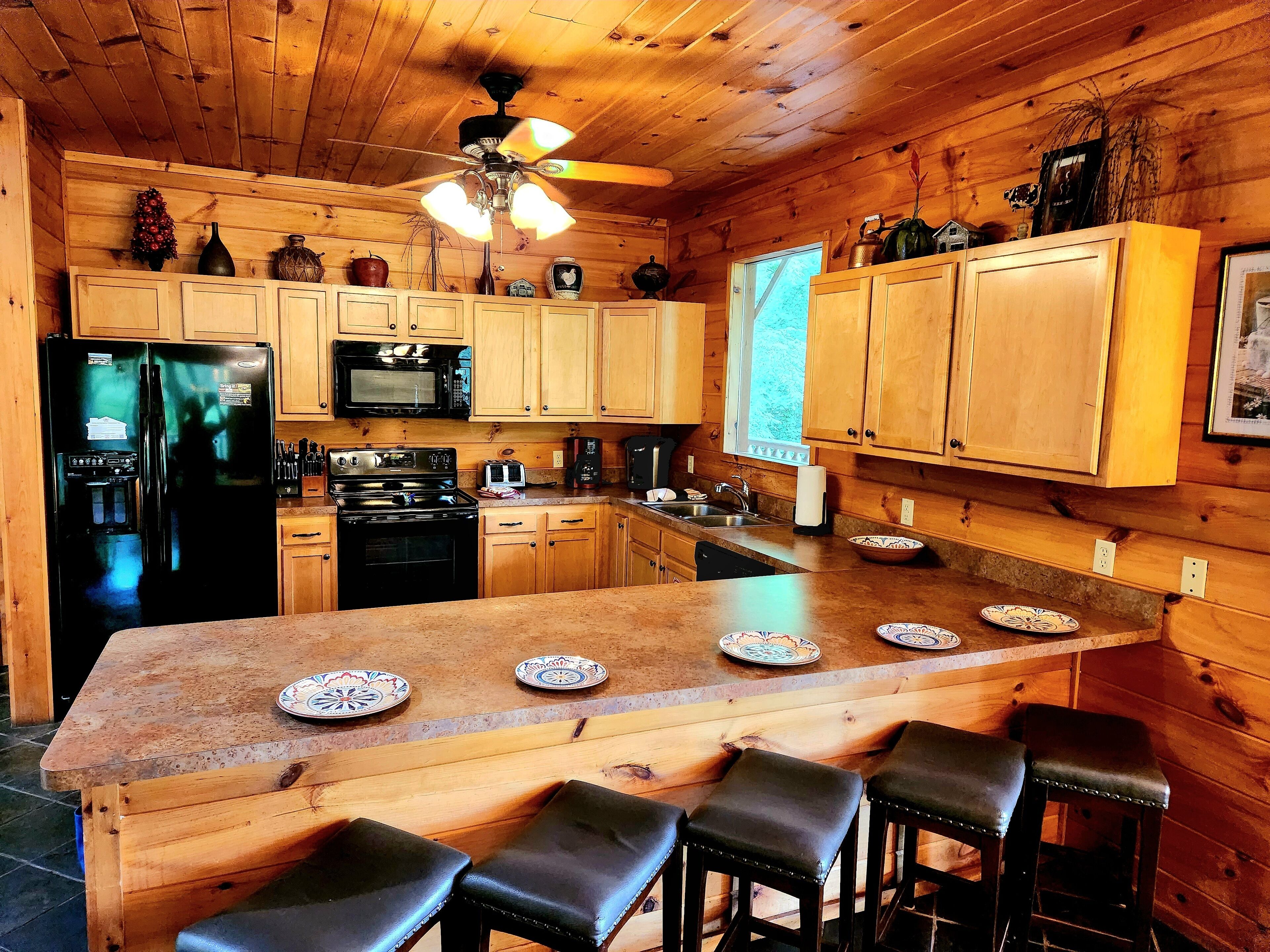 A wooden cabin kitchen with a refrigerator, stove, microwave, and a large island with bar stools.