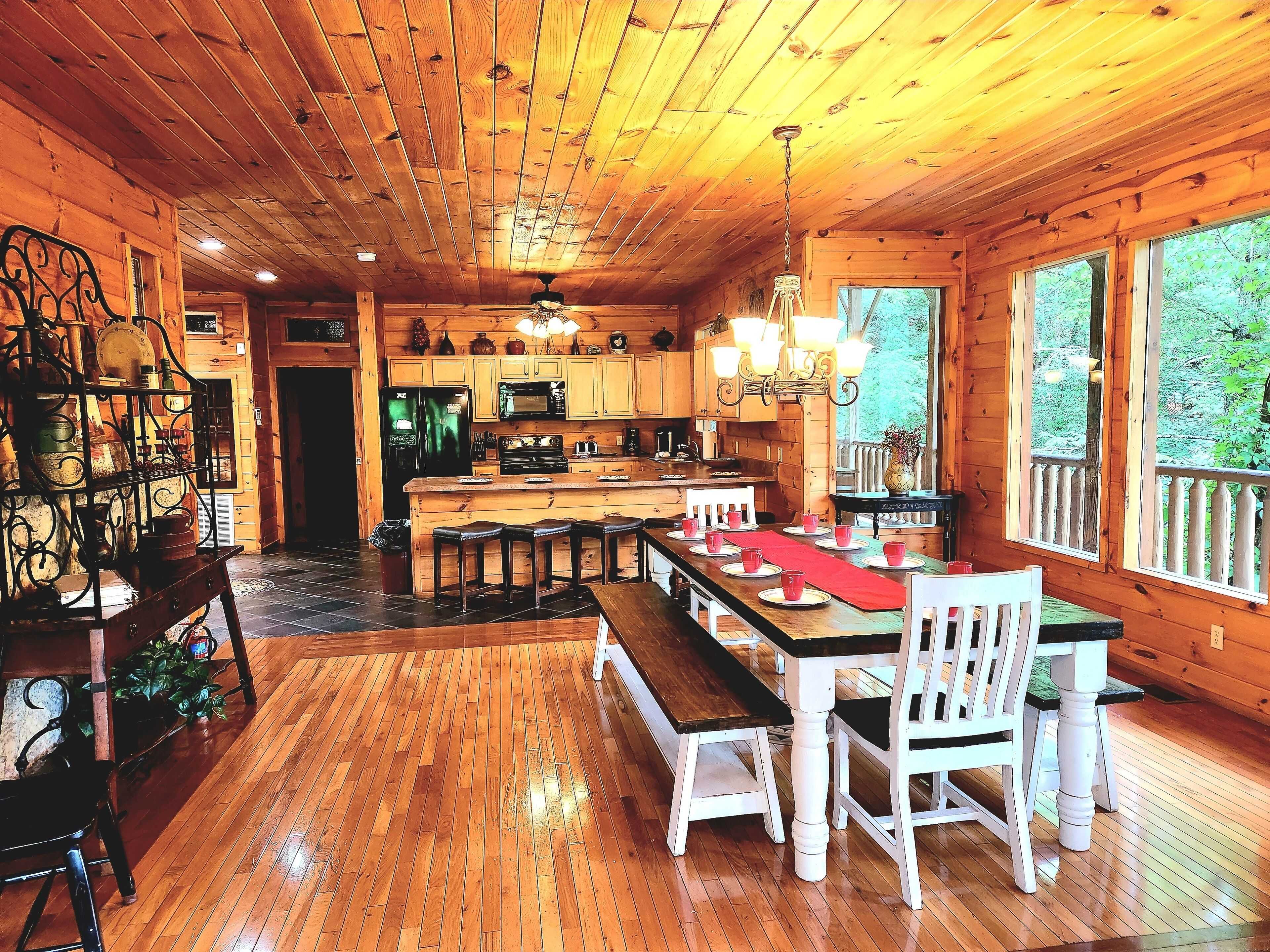 A wooden cabin interior with a kitchen, dining area, and large windows.
