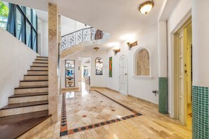Un amplio pasillo con una escalera de mármol, un balcón en el segundo piso y piso de baldosas.