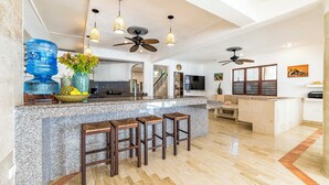 Eine großzügige Küche mit Granitabdeckungen, einer Bar mit Sitzgelegenheiten, Deckenventilatoren und einem großen Wasserspender.