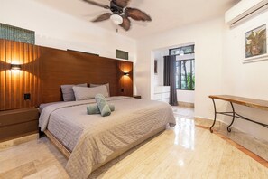 A bedroom with a large bed, wooden headboard, wall-mounted lights, a ceiling fan, and a view of the outdoors through a window.