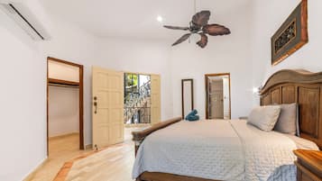 Une chambre à coucher avec un lit, une tête de lit en bois, un ventilateur de plafond et une vue sur un balcon.