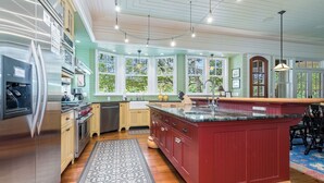 A modern kitchen with a large island, stainless steel appliances, and a view of the outdoors through large windows. - "Tupelo Honey" New Upscale Home With Magnificant Golf Course Views; screened in porch (Bald Head Island)
