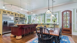 A spacious kitchen with a central island, bar stools, and a dining table with chairs. - "Tupelo Honey" New Upscale Home With Magnificant Golf Course Views; screened in porch (Bald Head Island)
