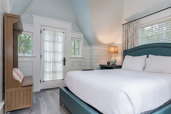 A bedroom with a large bed, a wooden bench, a nightstand, and a window with curtains. - "Tupelo Honey" New Upscale Home With Magnificant Golf Course Views; screened in porch (Bald Head Island)