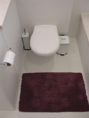 Een kleine, functionele badkamer met een wit toilet, een prullenbak en een toiletrol aan de muur.