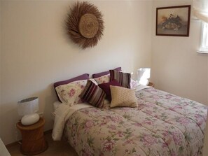 Een slaapkamer met een bloemenbedekker, een geweven wanddecoratie en een ingelijst kunstwerk aan de muur.