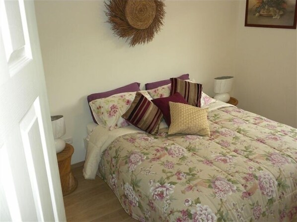 Een slaapkamer met een bloemenbedekking, meerdere kussens, een wandkleed van geweven materiaal en nachtlampjes.