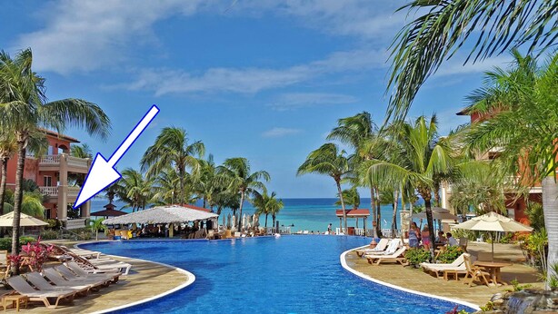 A resort pool area with lounge chairs, palm trees, and a view of the ocean. - ONLY Beachfront Suite @ Infinity Bay Resort - 24hr Service, Pools, Spa, Luxury! (West Bay Beach)