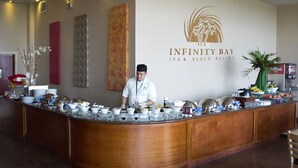 A buffet counter with a variety of dishes and a staff member standing behind it. - ONLY Beachfront Suite @ Infinity Bay Resort - 24hr Service, Pools, Spa, Luxury! (West Bay Beach)
