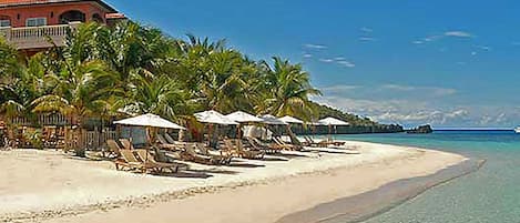 A beach with sun loungers and umbrellas, a building with a red roof, and a clear blue sky.