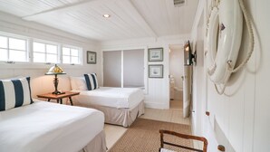 A room with two beds, a wooden nightstand, a lamp, a framed picture, a whiteboard, and a telephone. - Oceanfront Historic Beach Cottage | Steps from Beach (Tybee Island)