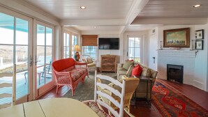 A spacious living room with a large window, a fireplace, and a television. - Oceanfront Historic Beach Cottage | Steps from Beach (Tybee Island)