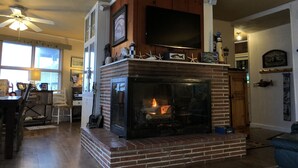 Una sala de estar con chimenea, un televisor montado encima y un ventilador de techo.