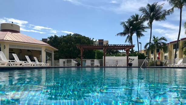A clear swimming pool with lounge chairs and a covered area, surrounded by palm trees and buildings. - Work remote, or not at all, in paradise at this cozy, beachy condo!  (Tavernier)