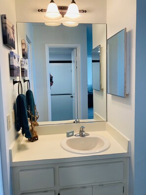 A bathroom with a white sink, a mirror, and a door leading to another room.