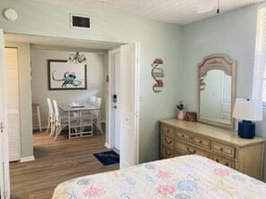 A bedroom with a bed, dresser, mirror, and a dining area with chairs and a table.