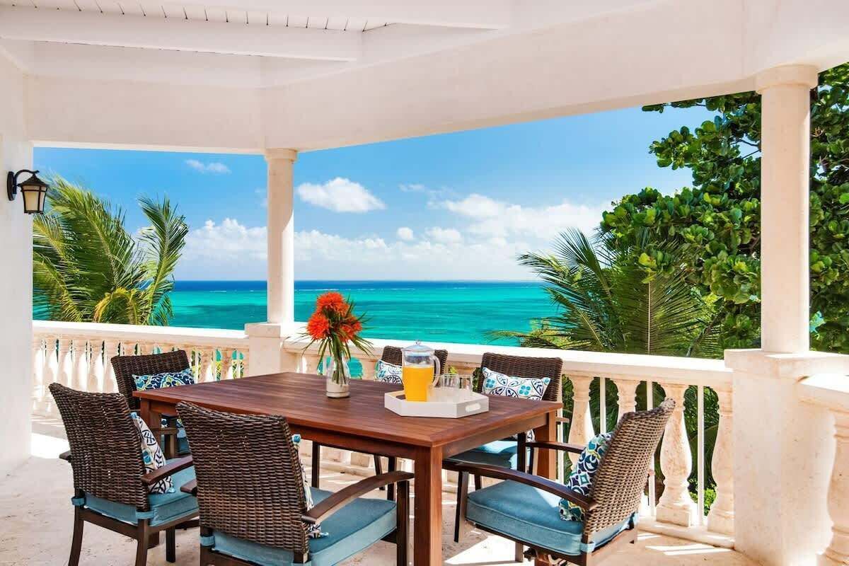 Ein überdachter Außenbereich mit Tisch, Stühlen und Blick auf das Meer.