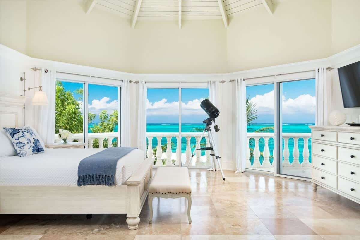 Ein Schlafzimmer mit einem großen Bett, einer Bank, einem Teleskop und einem Balkon mit Meerblick.