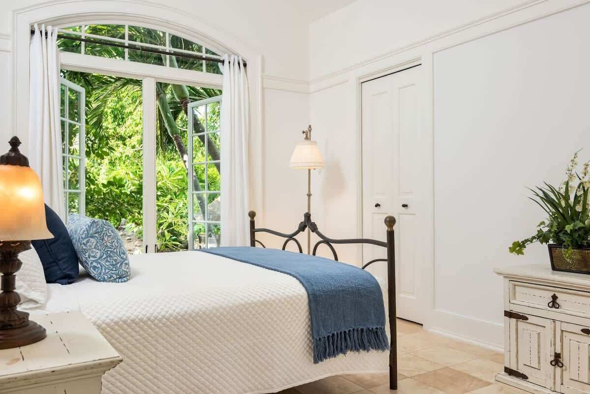 A bedroom with a bed, a nightstand, a lamp, a window with curtains, and a door.