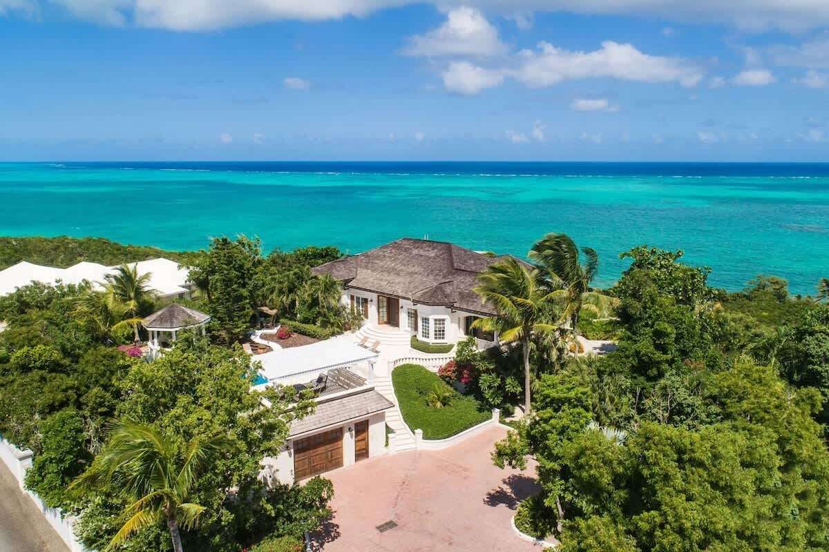 A large house with a pool, surrounded by lush greenery and a view of the ocean.