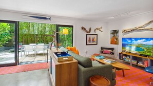 A modern living room with a sofa, coffee table, and TV. There is a bookshelf with books and a painting. A dining area with chairs and a table is visible through a glass door. - Coconut Grove Dream, located in the heart of the village. Beloved by the sailors (Miami)