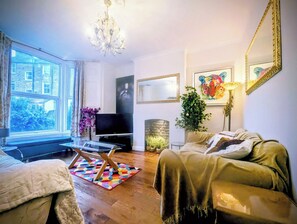 A living room with a sofa, a television, a chandelier, and a large window. - Amazing very spacious quiet convenient garden apartment in central London (London)