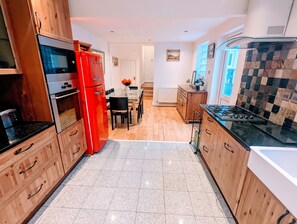 A kitchen with wooden cabinets, a red refrigerator, a dining table with chairs, and a tiled backsplash.