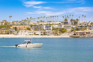 A coastal residential area with houses, a boat on the water, and a beach in the background. - Darling Balboa Island Getaway | Bay Views, Sunny Patio | Wildly Walkable - No Car Needed! (Newport Beach)