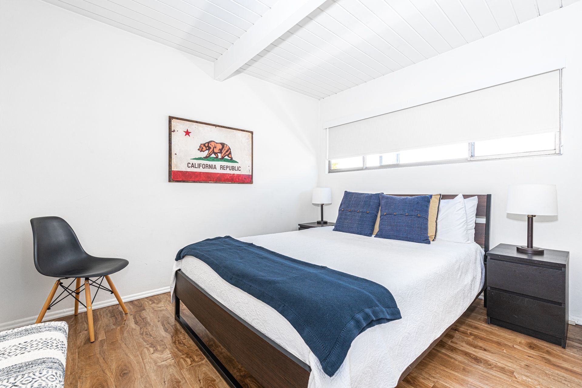 A bedroom with a bed, bedside tables, a chair, a rug, a wall-mounted picture, and a window.